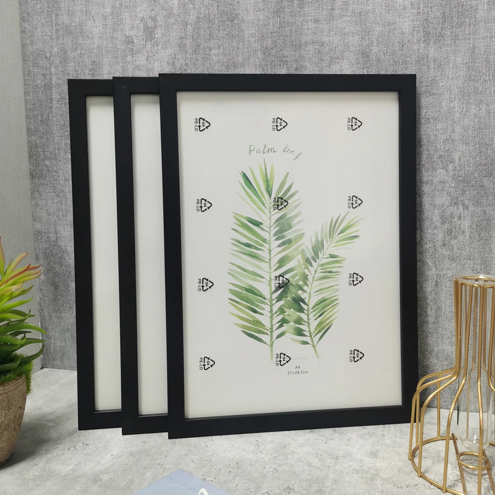 A set of three black wooden photo frames displaying green palm leaf watercolor designs on white paper.