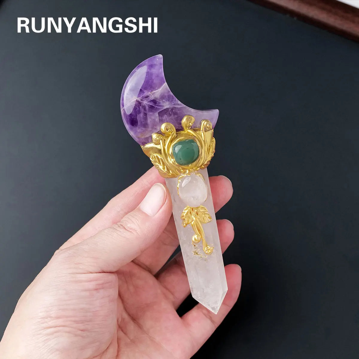 A hand holds a natural crystal moon and star scepter wand featuring purple amethyst, green jade, and gold accents.