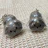 A pair of silver-toned rabbit hair keepsakes or keychains resting on a beige woven fabric surface.