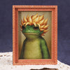 A cute green frog illustration framed in a wooden photo frame.