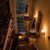 A dark, shimmering witch hat chandelier with hanging star tassels illuminates a hallway.