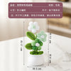 A hand-woven crochet flower in white and green is potted in a white ceramic container.