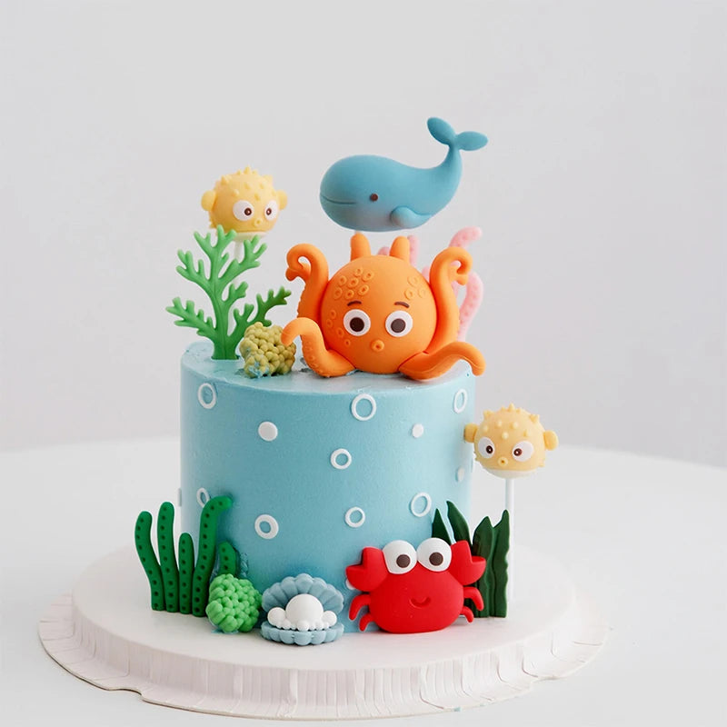 A tiered cake decorated with ocean animal toppers including a blue whale, an orange octopus, and a pink turtle.