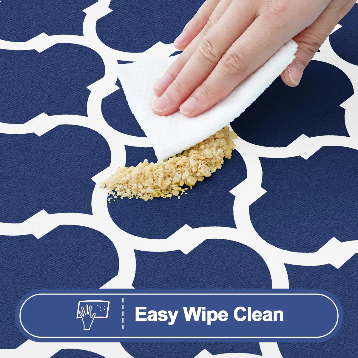 A hand wipes a textured cleaning pad on a dark blue patterned tablecloth.