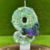 A decorative number eight made of green and iridescent sequins, featuring a purple butterfly, displayed on a white stand.