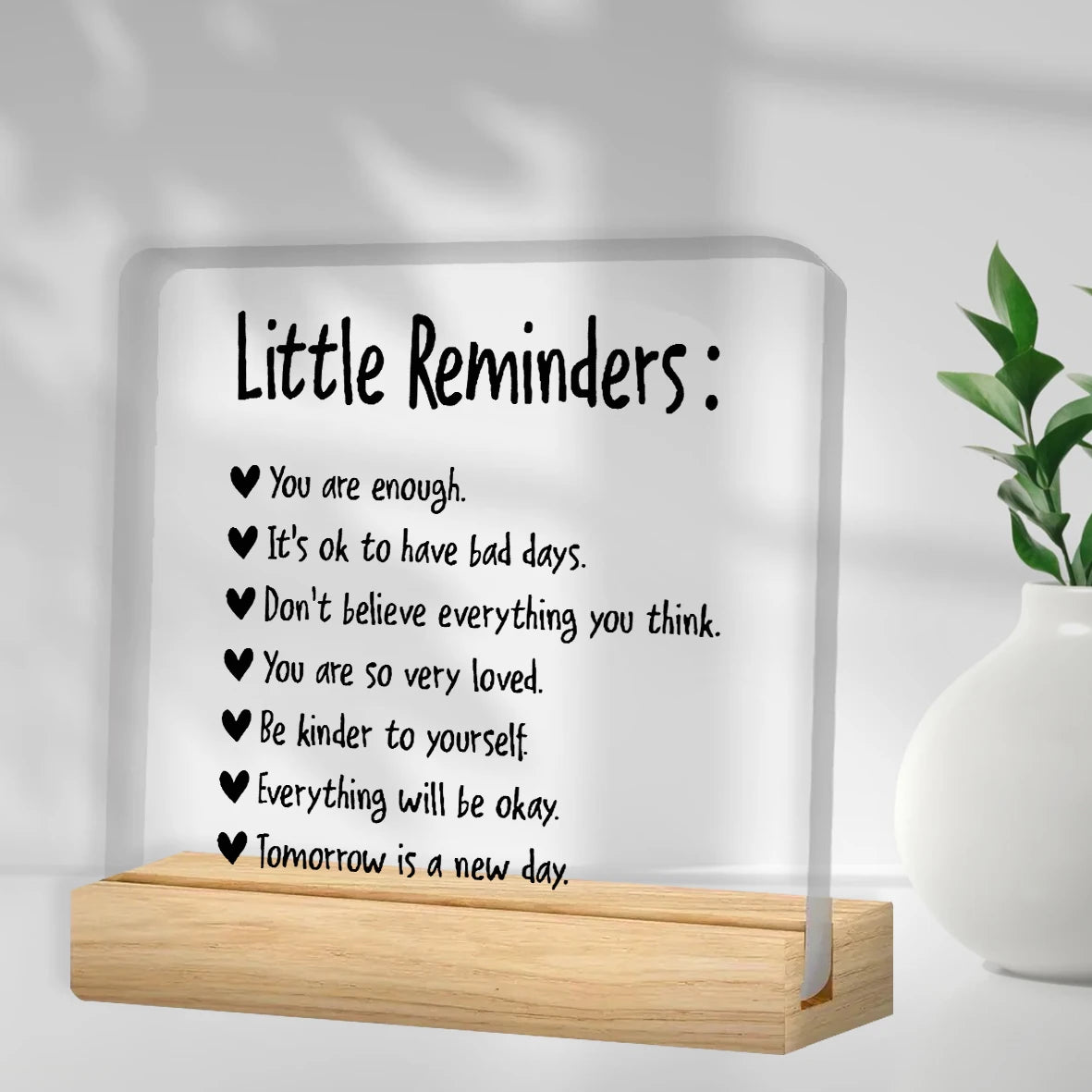 A clear acrylic desk plaque with black text listing positive affirmations like You are enough and Be kinder to yourself.
