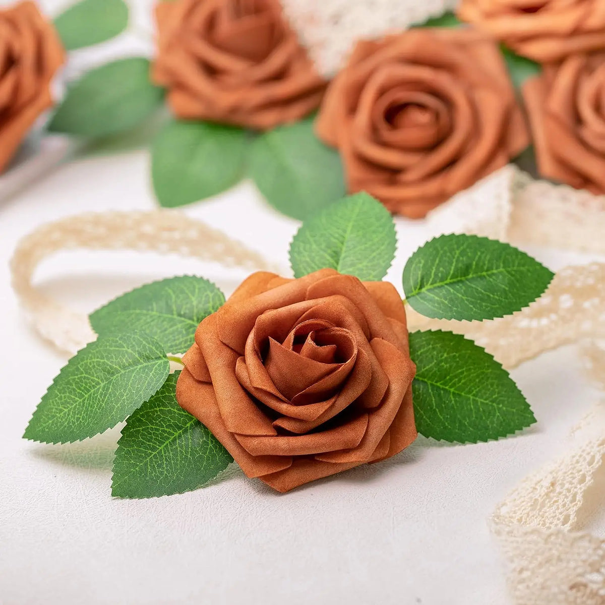 A cluster of artificial real touch foam roses in various shades of brown and green leaves on a white background.