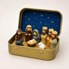 A miniature nativity scene featuring figures and a lamb is displayed inside a gold-colored metal box under a starry blue back
