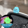 A glowing blue resin chicken ornament is shown on a black surface, with a green version in a hand nearby.