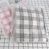 A plaid fabric storage bag filled with folded clothing, displayed on a grid background.