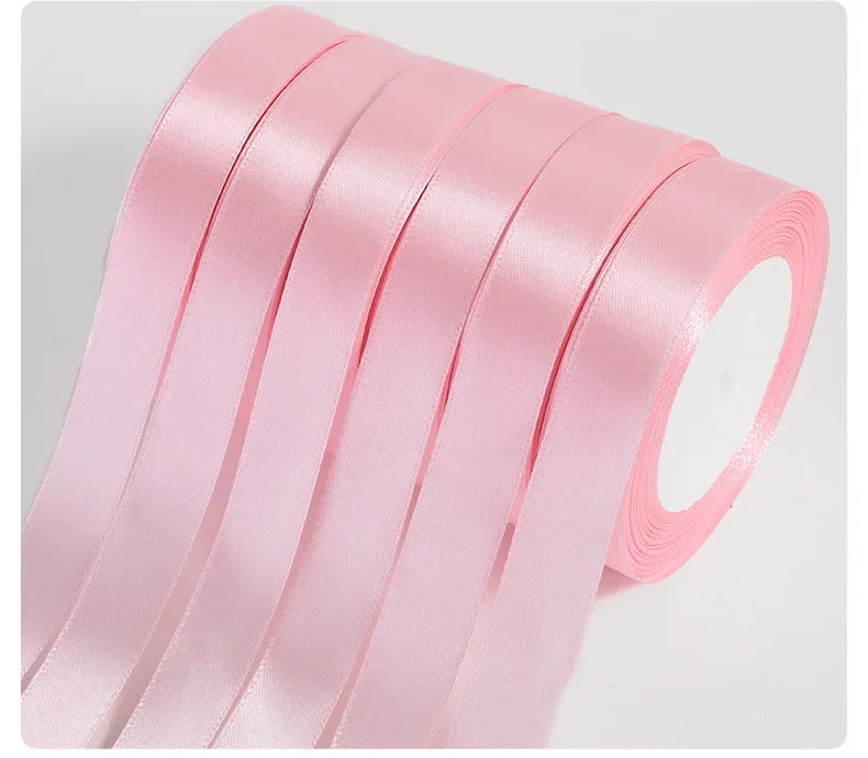 A stack of pink silk satin ribbons rolled and stacked for crafting.