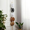 Macrame hat hangers in white and black hanging on a white wall next to a large green plant.