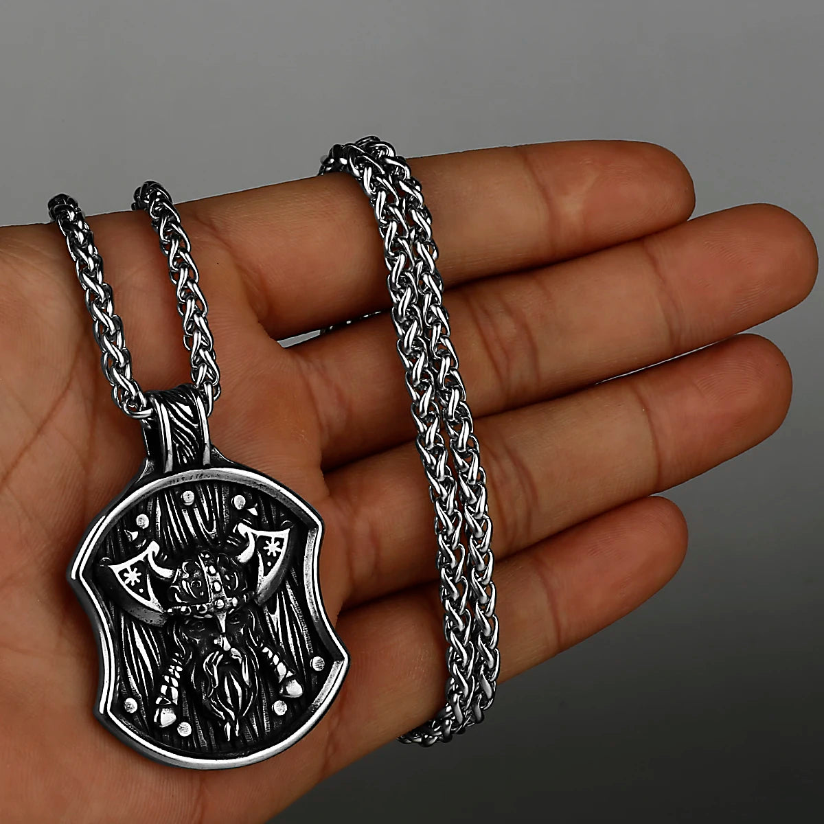 A stainless steel Viking warrior shield pendant on a silver chain held in a hand.