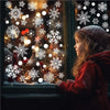 A young girl looks through a window decorated with white snowflake clings and holiday lights.