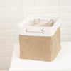 A beige fabric storage cube with a white metal frame and a woven handle, holding small white items.