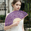A woman holds a purple vintage lace hand fan with a tassel pendant against a blurred outdoor background.