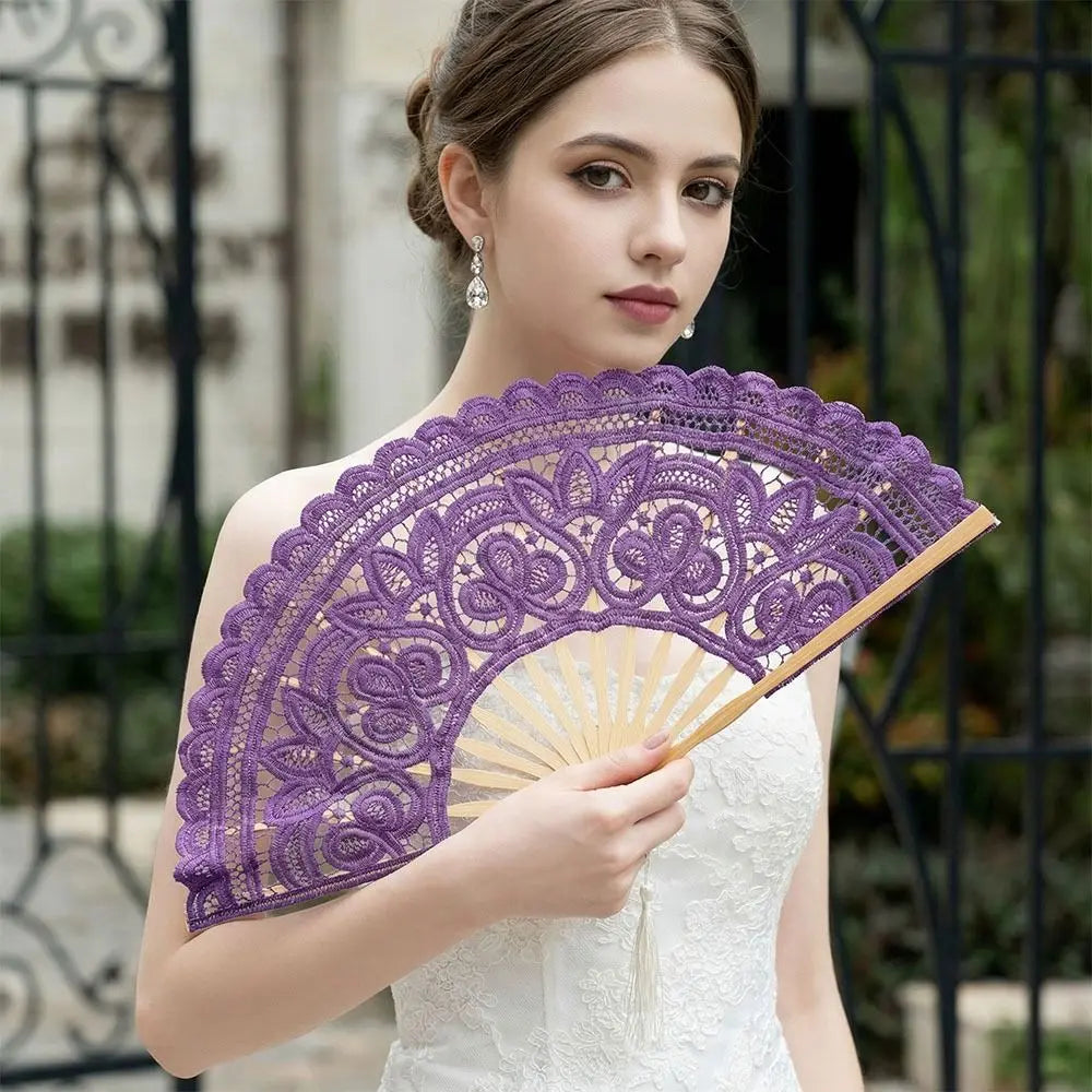 A woman holds a purple vintage lace hand fan with a tassel pendant against a blurred outdoor background.