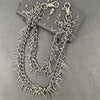 A silver chain necklace featuring sharp metal rivets and spikes, displayed on a dark surface.