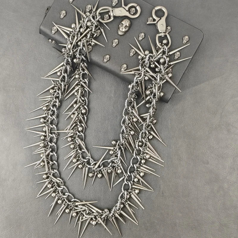 A silver chain necklace featuring sharp metal rivets and spikes, displayed on a dark surface.