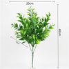A tall artificial fern plant with green leaves displayed in a clear glass vase.