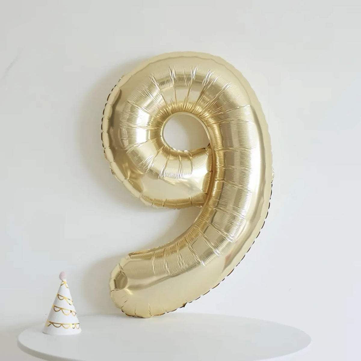 A large gold foil number balloon shaped like the number 9 is displayed against a white background.
