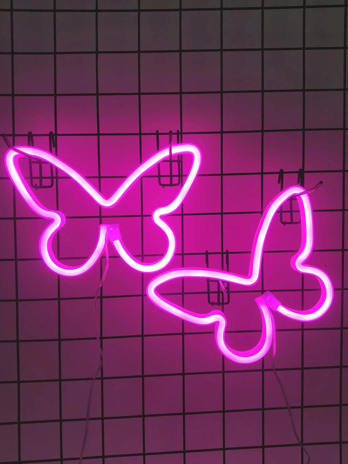 A pink neon sign shaped like a butterfly is mounted on a grid background.