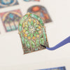 A die-cut sticker shaped like a stained glass window featuring green and yellow floral patterns.