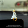 A white resin cartoon duck figurine with yellow feet is displayed on a dark surface.