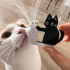 A white cat is blowing whiskers onto a black acrylic cat silhouette with a white vase.