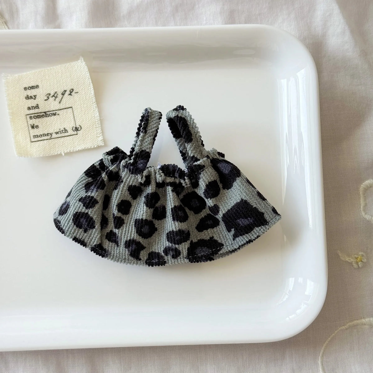 A dark gray leopard print shoulder strap skirt is displayed on a white plate next to a small note.