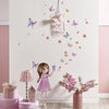 A pink-haired girl figurine stands in front of a white wall decorated with butterfly stickers and floral accents.