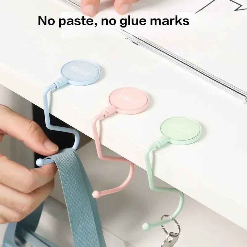 Hand holding a light blue purse hook with a strap, demonstrating no paste or glue marks on the white surface.