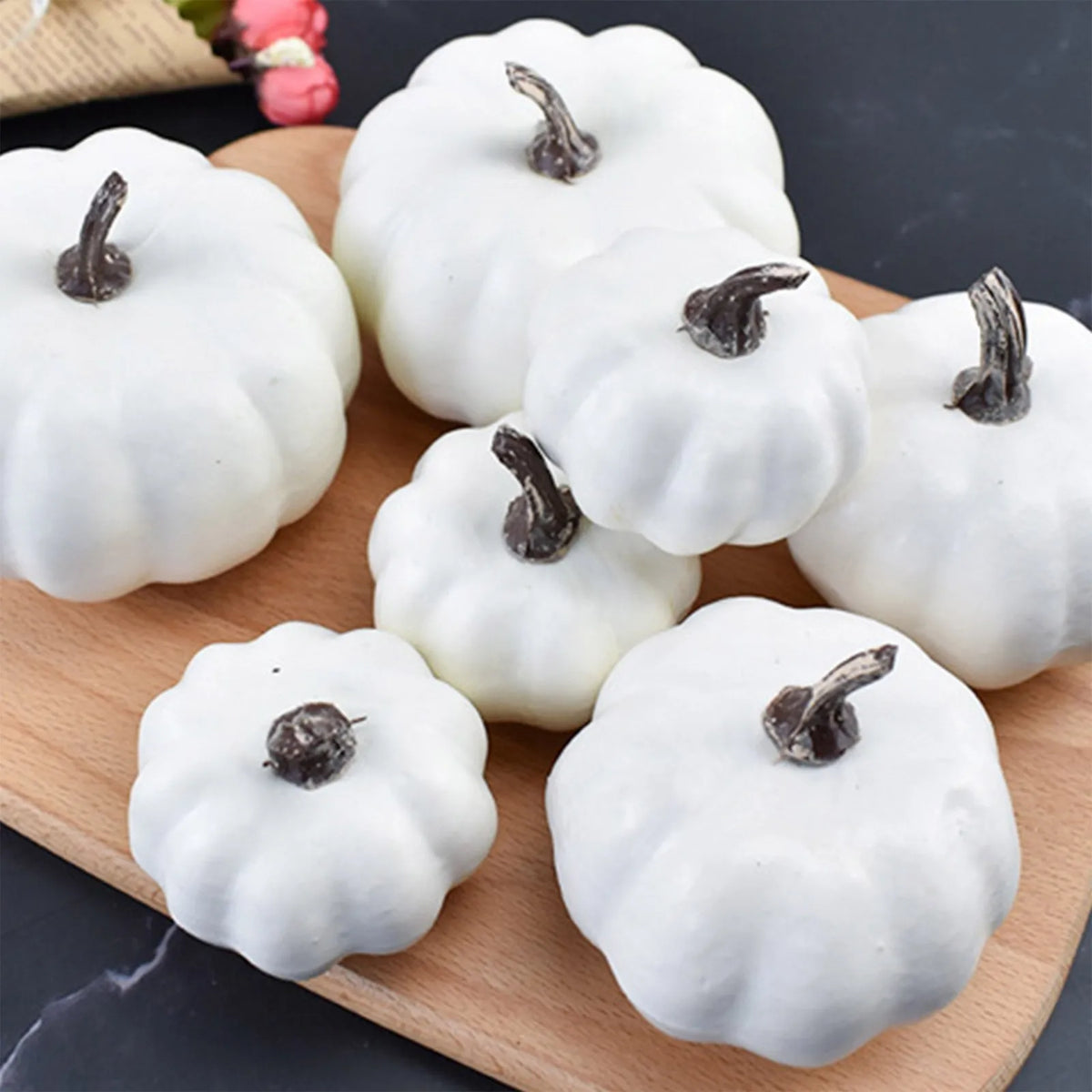 A set of seven white artificial pumpkins arranged on a wooden board for fall and Halloween decoration.