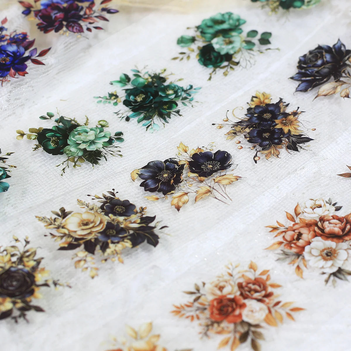 A collection of floral PET sticker rolls in various shades of green, blue, purple, and gold scattered on white paper.