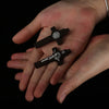 A hand holds a dark wooden St. Benedict crucifix pendant against a black background.