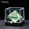 A clear box displays a green fluorite crystal specimen on a black surface.
