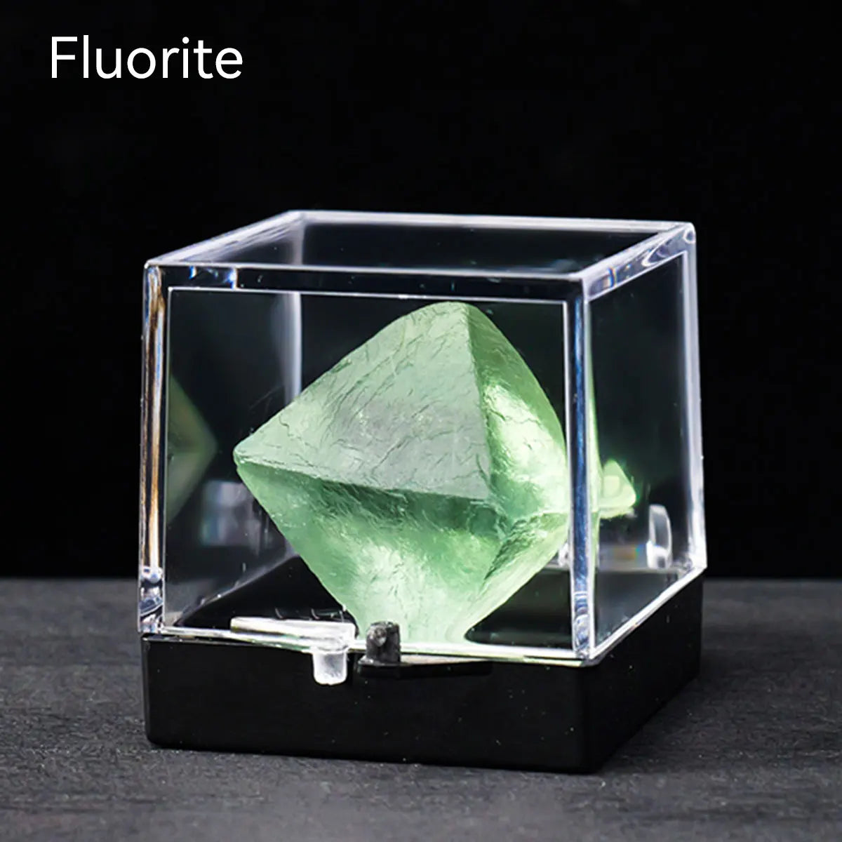 A clear box displays a green fluorite crystal specimen on a black surface.