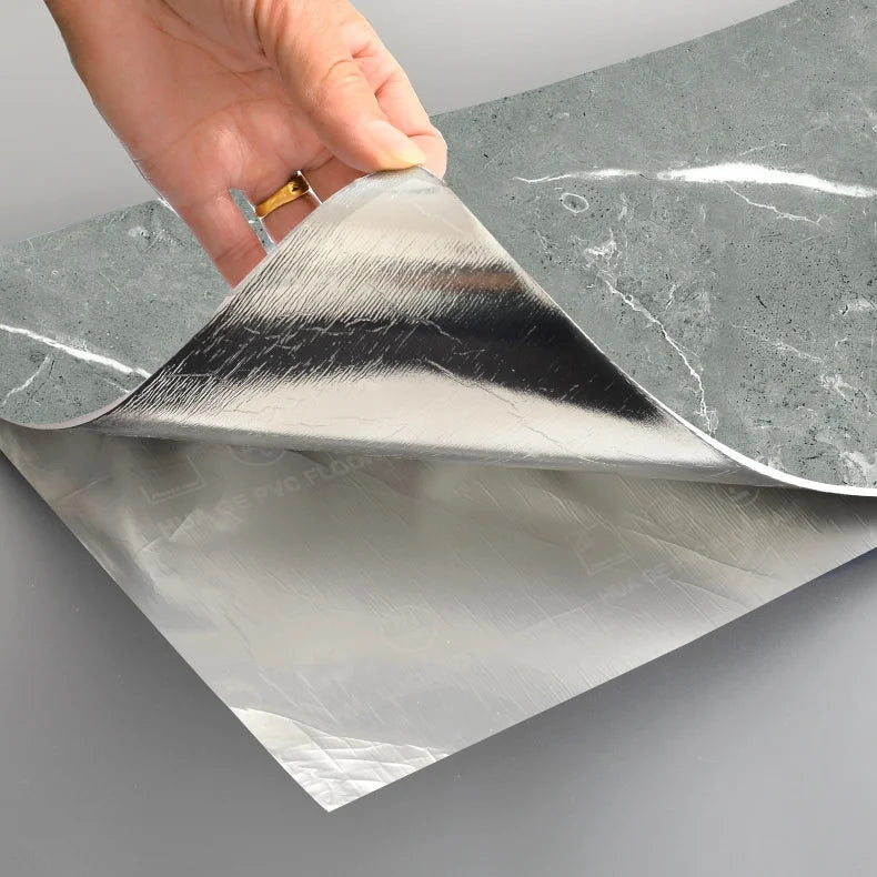 A hand is peeling a sheet of self-adhesive marble wall tiles from its backing paper.