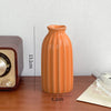 An orange ceramic bud vase with a glossy finish sits on a wooden surface.