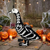 A black and white skeleton goose lawn decor statue with a long neck standing on a stone path surrounded by autumn leaves.
