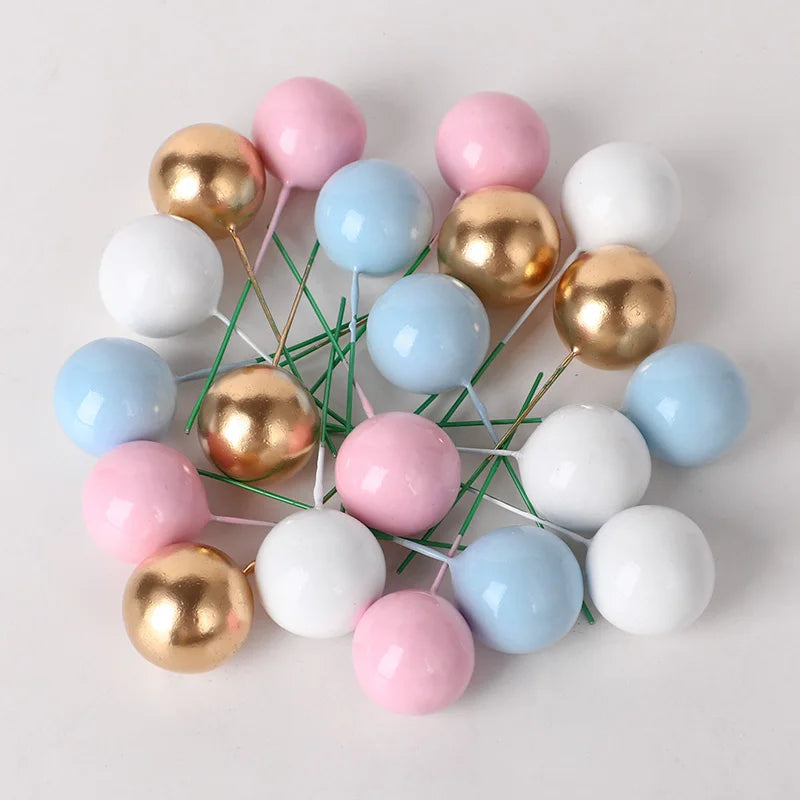 A collection of colorful spherical cake toppers in pink, white, and gold metallic finishes arranged on a white background.
