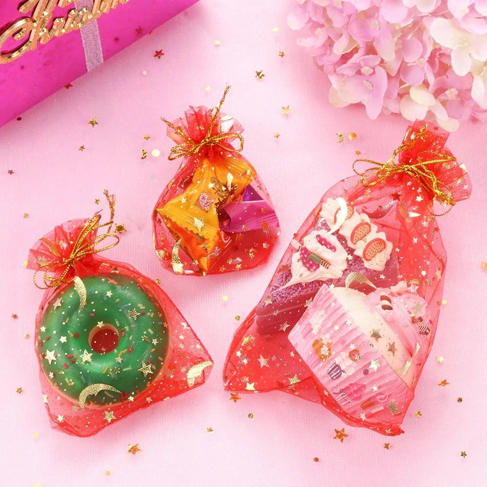 Red organza drawstring bags filled with glitter and featuring moon and star patterns on a pink background.