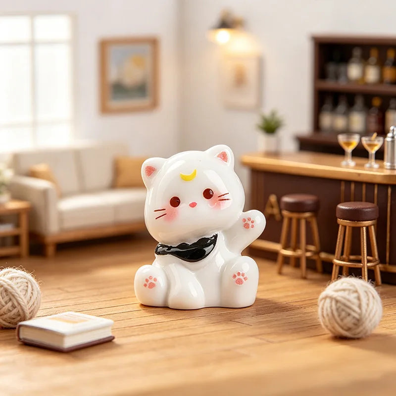 A white resin cat keychain with pink accents sits on a wooden table next to a ball of yarn.