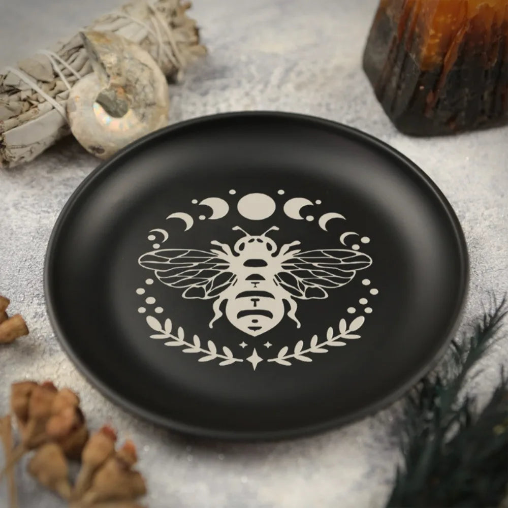 Assiette en céramique noire avec une silhouette de guêpe blanche entourée de lunes et de feuilles.