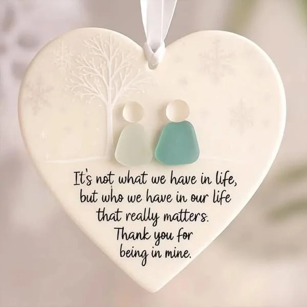 A white heart-shaped ornament featuring a frosted tree design and two small, pale green keepsake pendants.