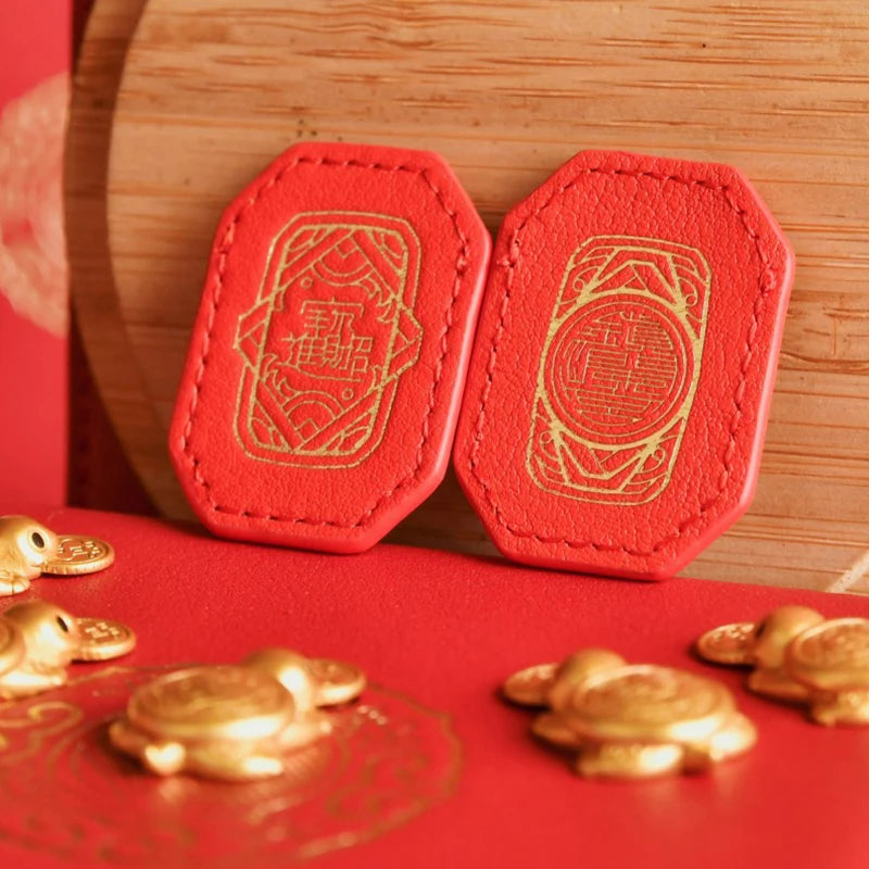 Two orange-red hexagonal tiles featuring gold-colored patterns, displayed on a red surface.