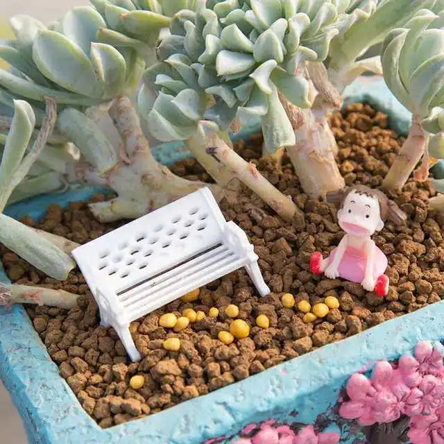 A close-up of a succulent plant in a pot surrounded by granular slow-release fertilizer and a small pink figurine.