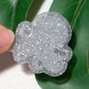 Silver glitter acrylic charm shaped like a cloud being held by a finger against a green leaf background