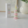 A tall, stacked candle holder with pastel pink and green candles and a decorative topper on a white box.