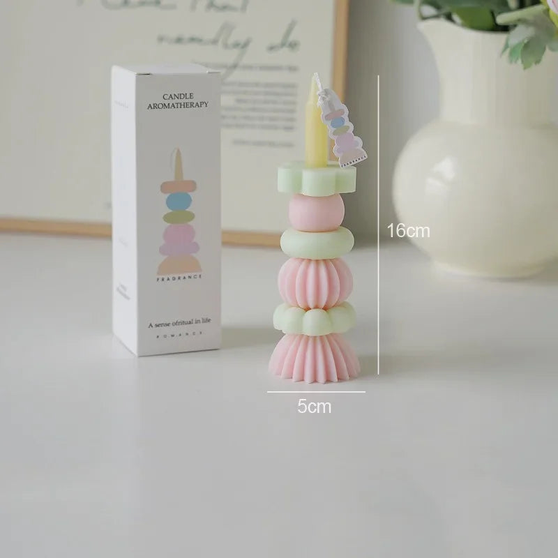 A tall, stacked candle holder with pastel pink and green candles and a decorative topper on a white box.